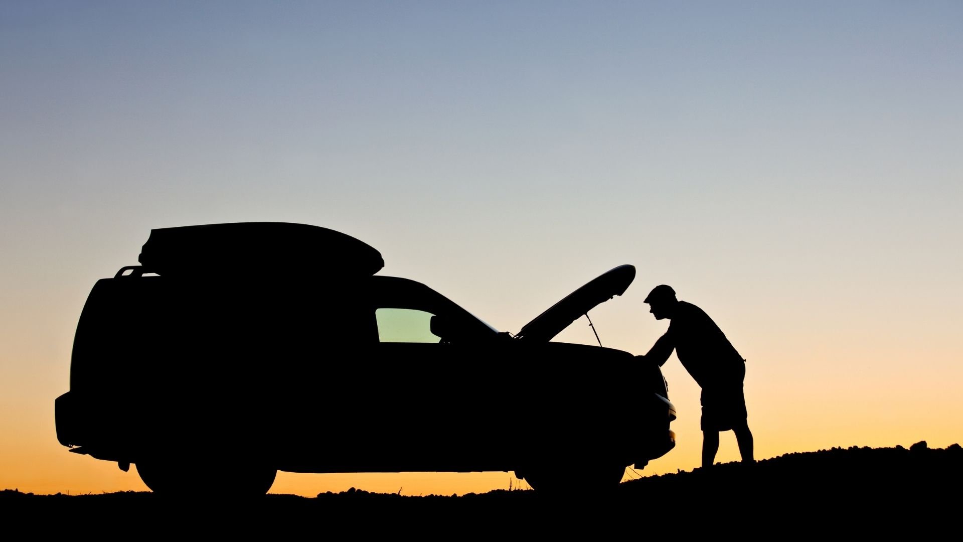 Silhouette of person checking car engine at sunset or sunrise