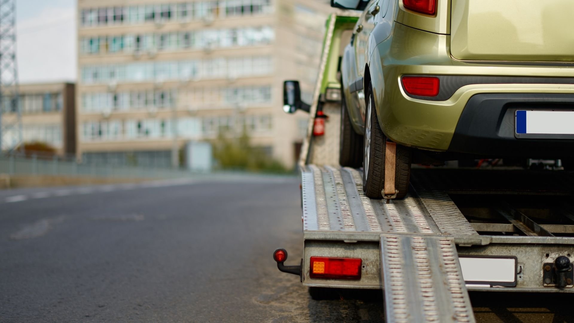 Green car being loaded onto a metal tow truck ramp in urban setting