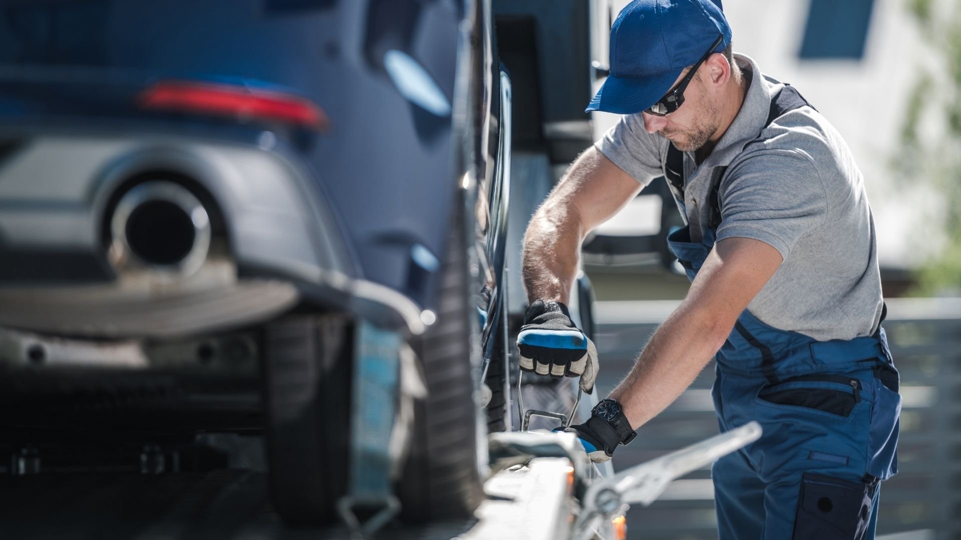 Automotive technician changing tire wearing blue cap and work gloves