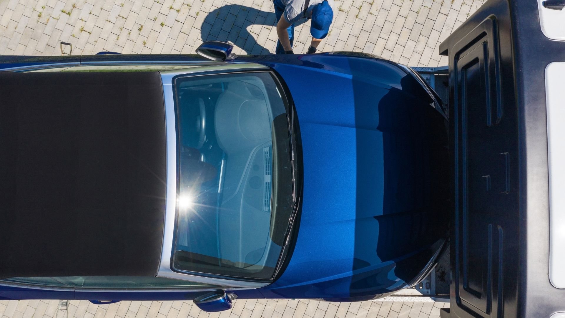 Blue electric car viewed from above with open door on brick pavement