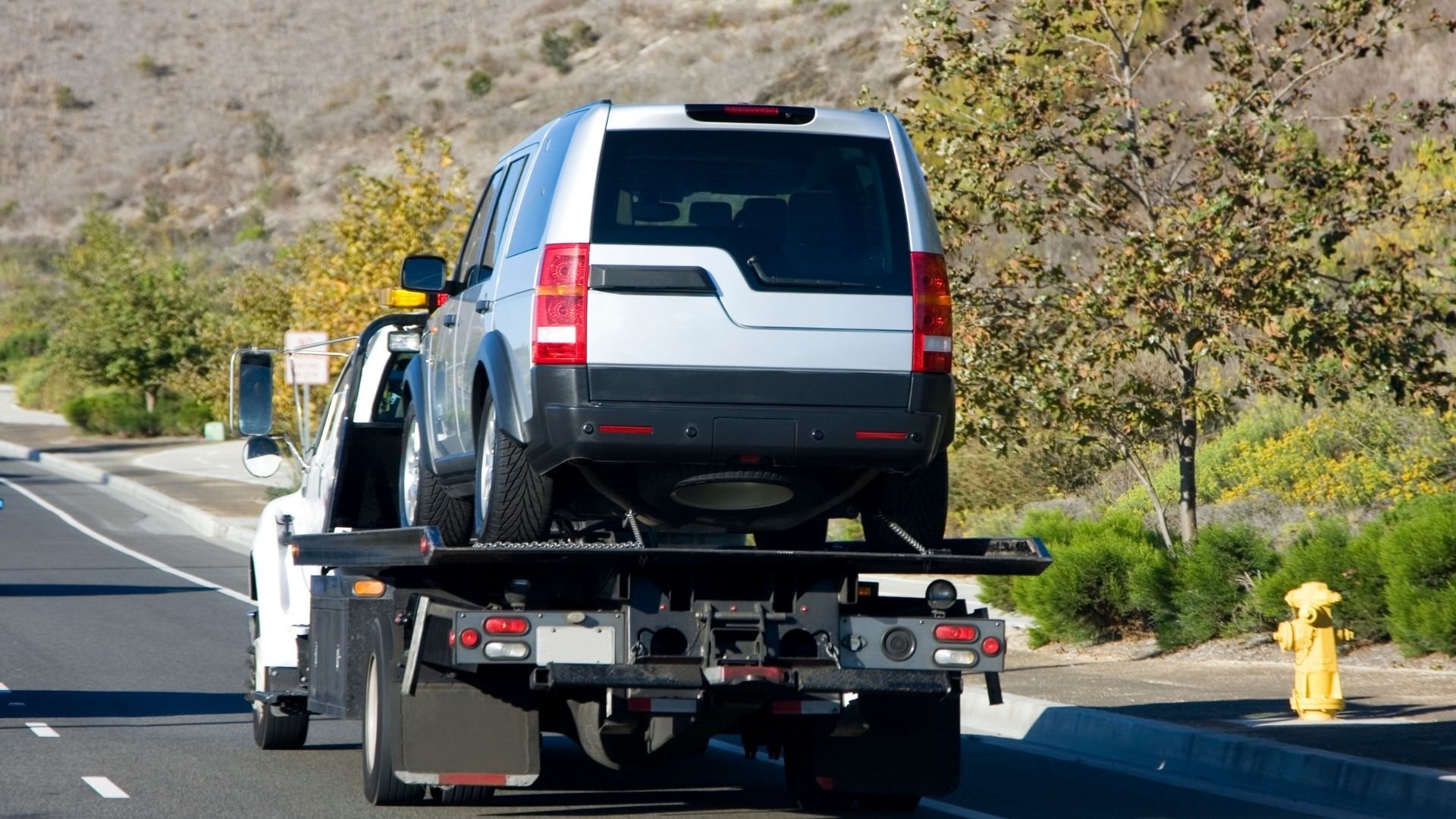 White SUV being towed on a flatbed truck along a winding road