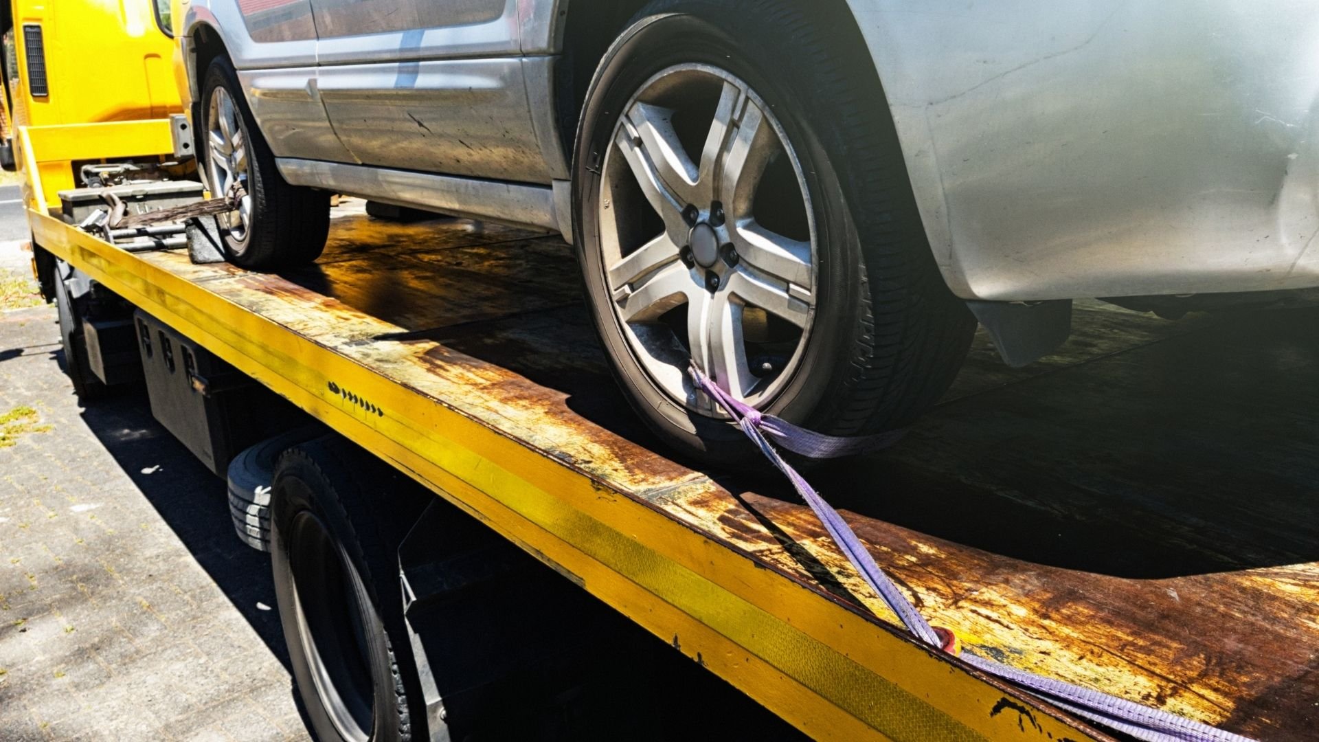 Silver car secured on yellow tow truck with purple straps